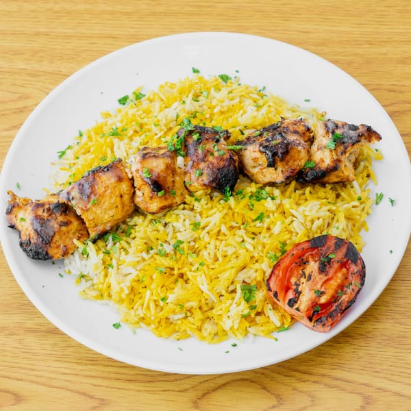 Grilled chicken skewer with yellow rice and a charred tomato half on a white plate.