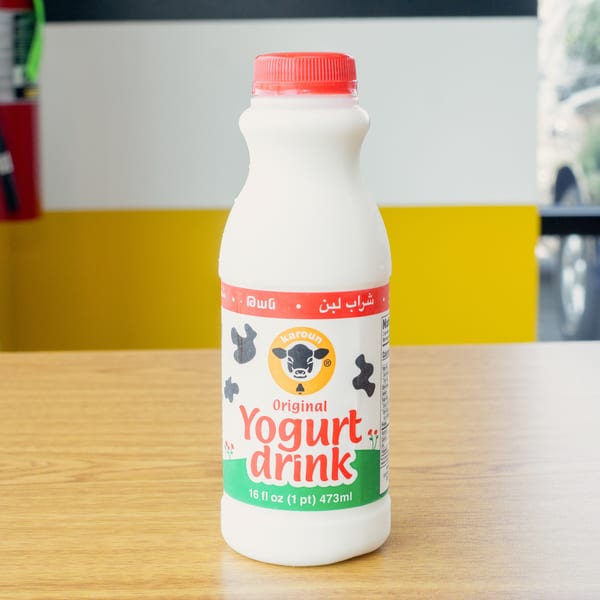 A bottle of Karoun Original Yogurt Drink with a red cap sits on a wooden table.