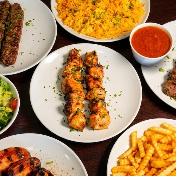 An overhead view of various Middle Eastern dishes including kebabs, rice, salad, and fries.