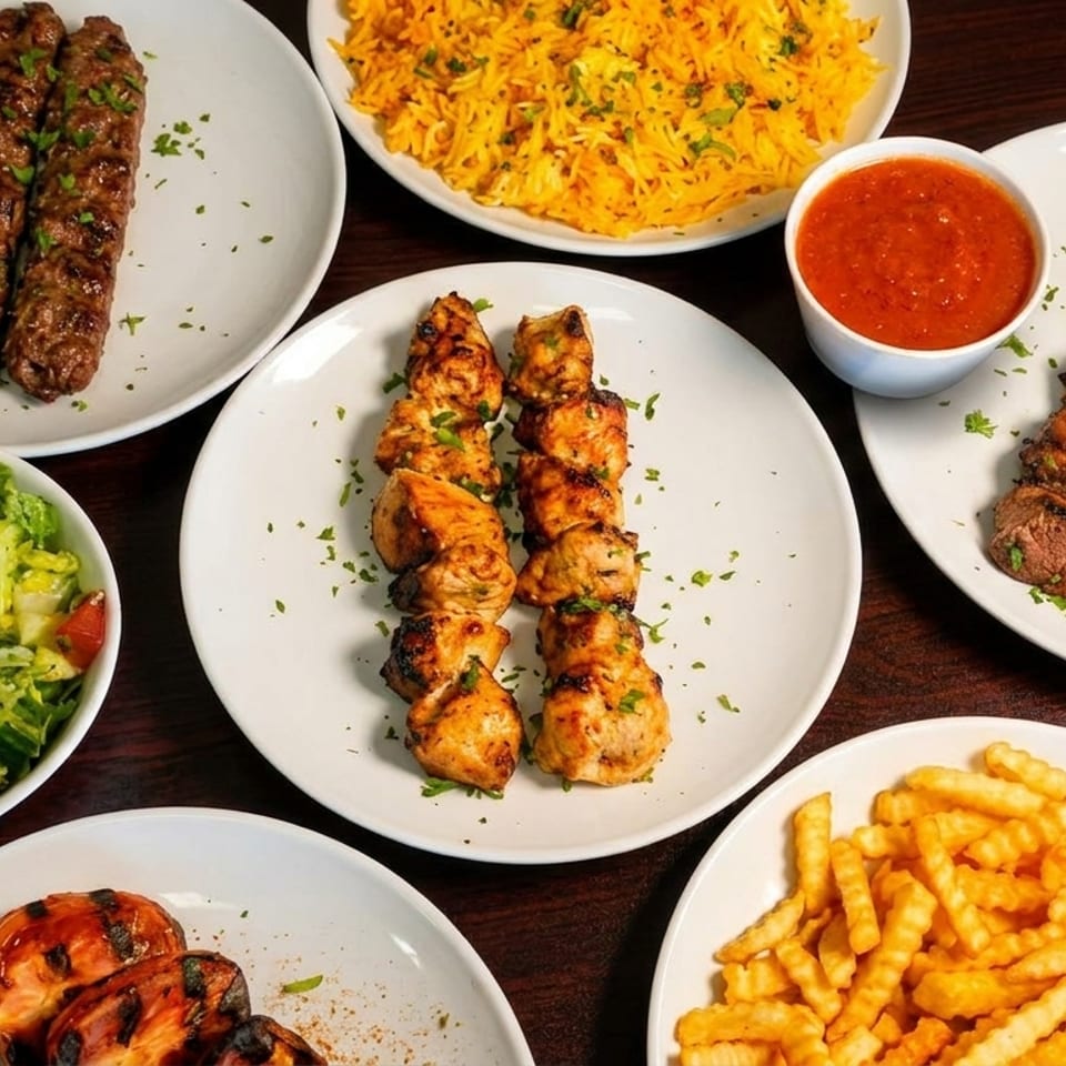 An overhead view of various Middle Eastern dishes including kebabs, rice, salad, and fries.