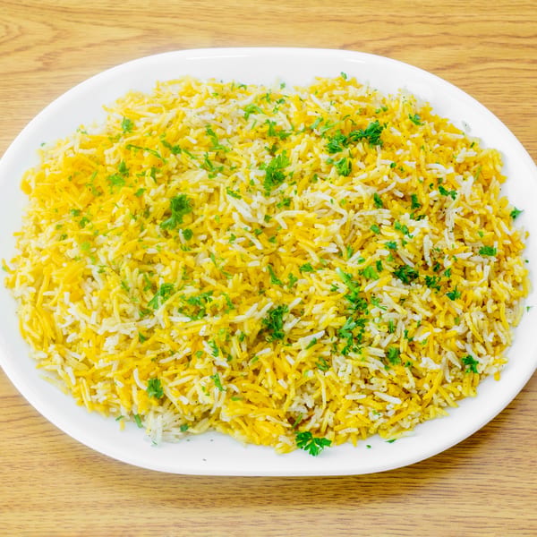 A white oval plate filled with yellow and white rice, garnished with fresh green parsley.