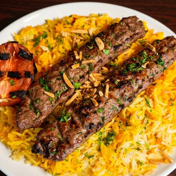 Two grilled meat skewers with rice, toasted almonds, parsley, and a grilled tomato on a white plate.