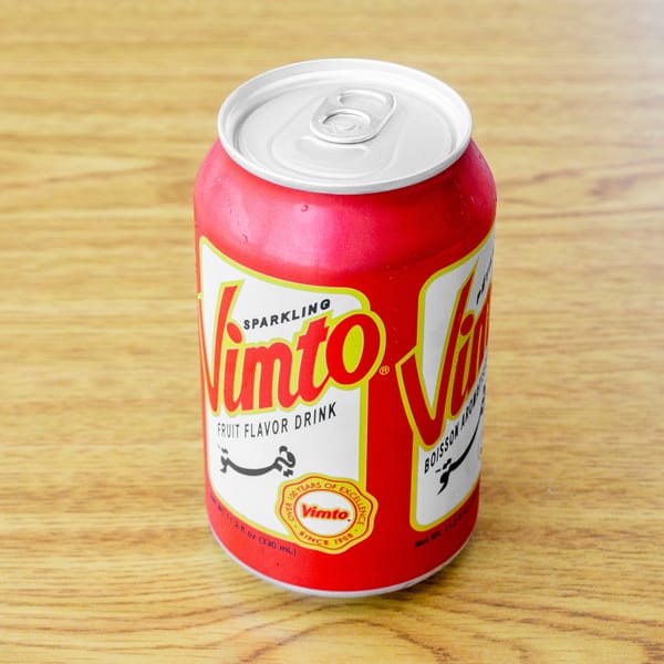 A red Vimto sparkling fruit flavor drink can with condensation sits on a wooden surface.
