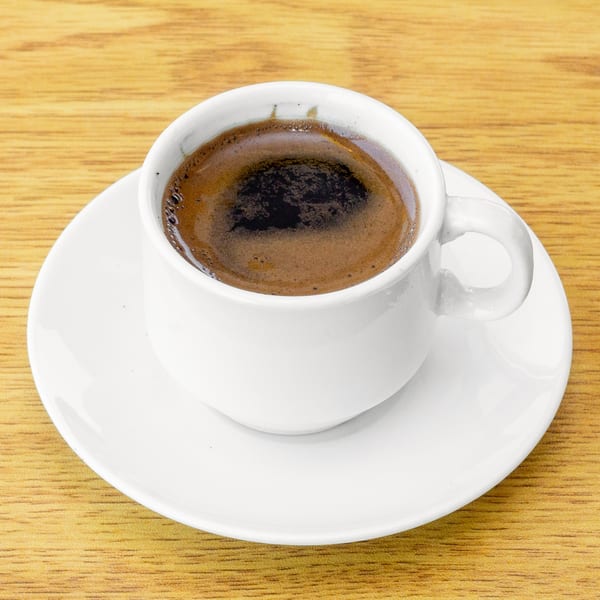 A white cup of dark Turkish coffee with foam on a matching saucer, on a wooden table.