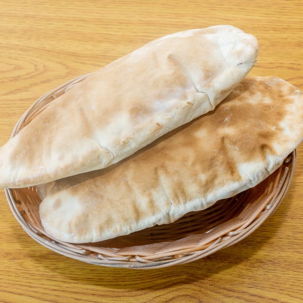 Two warm pita breads in a woven basket on a light wooden table.