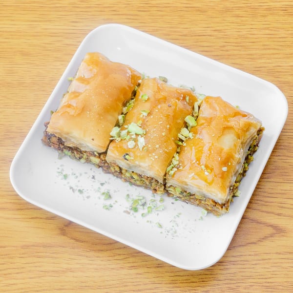Three pieces of golden baklava with chopped pistachios on a white rectangular plate.